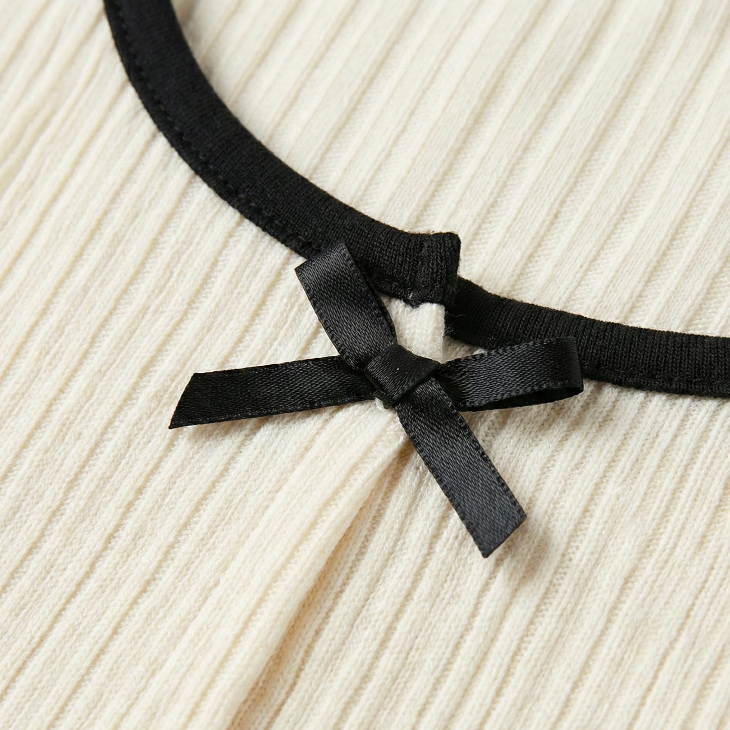 Ivory ribbed knit long-sleeve top featuring small black decorative bows down the center and on the sleeve cuffs.